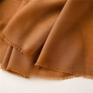 Detalle de bufanda color caramelo con textura suave de lino y bordes de flecos finos