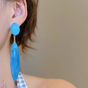 Close-up of long blue acrylic teardrop earrings on model with marble texture and gold metal