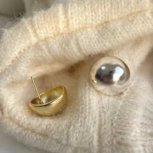 Close-up of matte gold and polished silver ball stud earrings on beige knit fabric