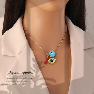 Gold chain necklace with evil eye, blue dice, and red pepper charms worn by a model