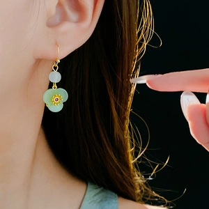 Detail of gold-plated flower earrings with green petals and white bead on model