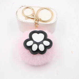 Pink faux fur pompom keychain with a black and white cat paw charm and golden hardware