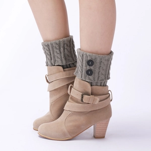 Detail of greyish-green knitted leg warmers with cable stitch and black buttons on boots