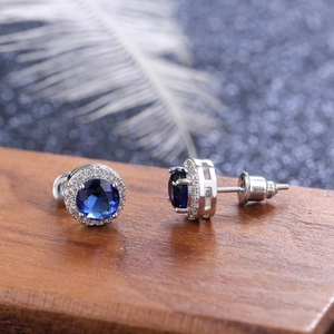 Macro view of round blue zircon stud earrings with silver pavé halo and butterfly back