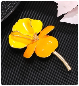 Macro detail of yellow enamel iris brooch with golden stem on black texture