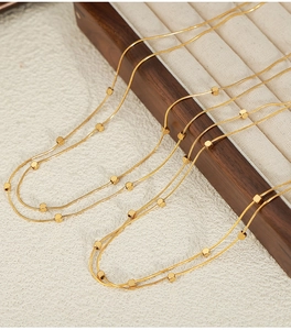 Detail of a golden snake chain necklace with small cubes on a wooden jewelry tray