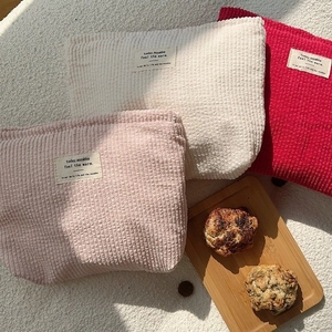 Three corduroy cosmetic bags in pink, beige and red on a white textured background