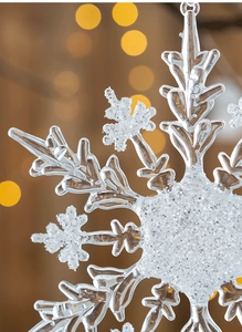 Macro shot of transparent acrylic snowflake ornament with white glitter and festive bokeh