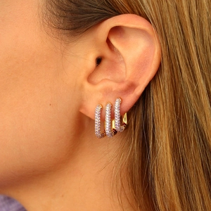 Macro shot of gold U-shaped earrings with purple zircon pavé settings on earlobe