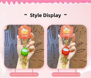 Close-up of red and green Maneki-neko Daruma bell charms with golden rings and blessing tags