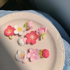 Detailed view of three cherry blossom hair clips in pink, white and red on a ceramic plate