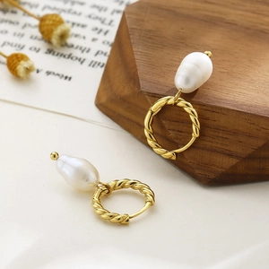Close-up of vintage gold twist hoop earrings with baroque pearls on a wooden display