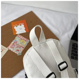 Detail of white corduroy backpack showing top handle and adjustable shoulder straps