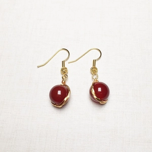 Gros plan sur des boucles d'oreilles en or 14K avec perles d'agate rouge et fil métallique