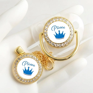 Close-up of golden pacifier with blue crown Prince text and rhinestone detailing