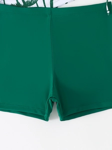 Detailed close-up of dark green swim shorts featuring tropical palm leaf print lining
