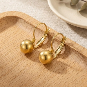 Detailed view of gold ball earrings with lever-back closure on a rustic wooden tray