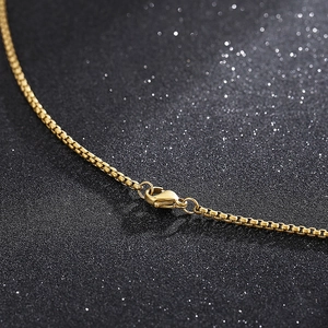 Macro detail of golden box chain necklace showing the polished lobster clasp and texture