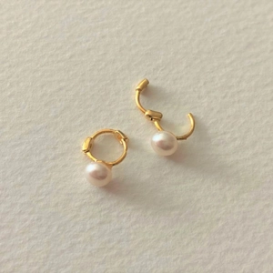 Detailed view of gold freshwater pearl hoop earrings on textured beige paper