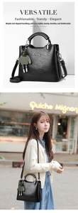Detail of black pebbled leather handbag with dual handles and green plush pendant charm