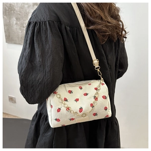 Detail of white corduroy shoulder bag with red strawberry print and golden chain strap