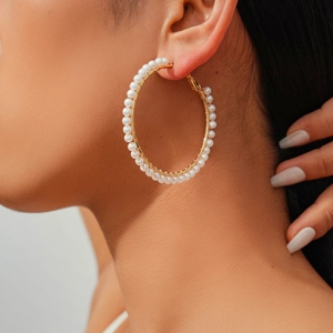 Detailed view of gold hoop earrings wrapped with small white pearls on a model ear