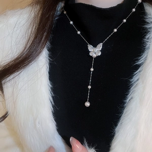 Dettaglio della collana con ciondolo a farfalla con nappe d'argento e perle su maglione