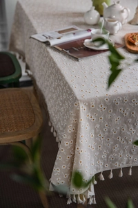 Detail of beige linen tablecloth with daisy embroidery and elegant fringe edges
