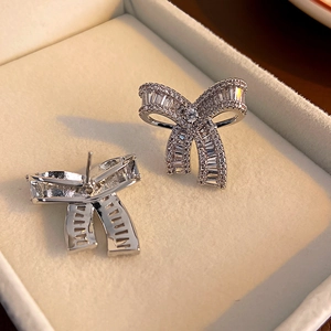 Macro detail of silver bow earrings with sparkling crystals on a textured jewelry box