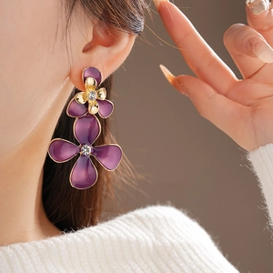Detailed view of large purple enamel flower earring with gold trim worn by a model