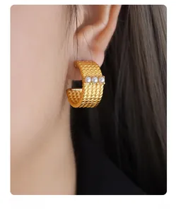 Macro shot of gold C-shaped twisted metal earrings with white pearl inlay on model