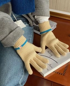 Detail of beige knit gloves with blue striped cuffs worn in a cozy lifestyle setting