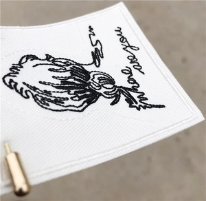 Macro shot of white embroidered fabric tag with black text and gold metal pin detail