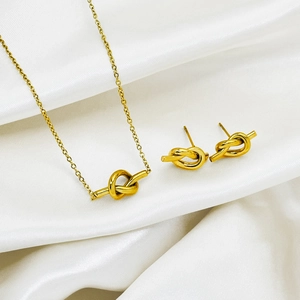 Minimalist gold knot jewelry set with necklace and stud earrings on white silk fabric
