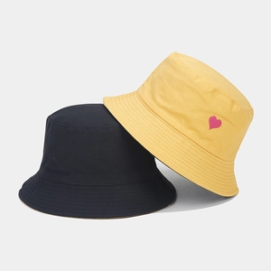 Détail de bobs en coton jaune et noir avec une petite broderie de cœur rose sur le côté