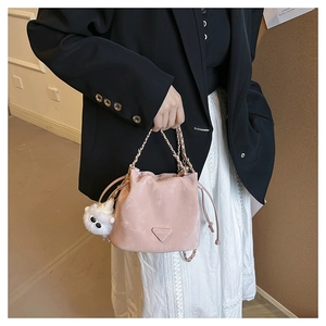 Pink drawstring bucket bag with gold chain strap and plush ball charm in hand