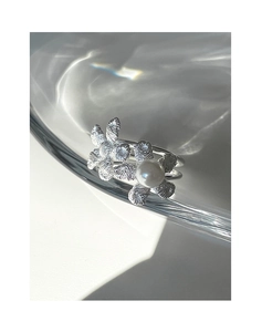 Detailed view of silver flower ring with pearl on a reflective water surface