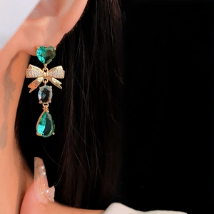 Macro detail of gold bow earring with green heart and teardrop zirconia stones