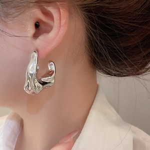 Close-up of silver irregular liquid lava style stud earring on model with metallic finish