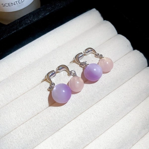 Detail view of purple and pink cat eye stone bead earrings with metal hooks on white velvet