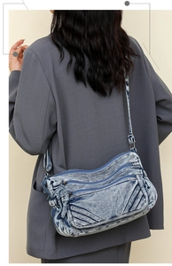 Detail of washed blue denim crossbody bag featuring multiple zipper compartments and texture