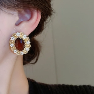 Detail of red oval gemstone earrings with white floral accents worn by a model