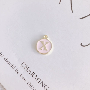 Detail shot of a round pink enamel pendant with gold letter X for DIY jewelry