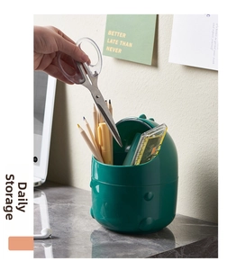 Deep green dinosaur desk trash bin used as a stationery organizer for pens and scissors