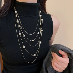 Close-up of multilayered gold pearl necklace with tiger eye stone on black turtleneck