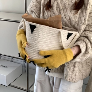 Detail of yellow knit gloves featuring black bows holding a woven storage basket