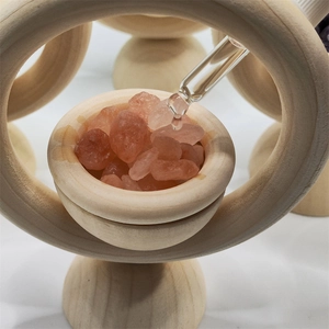 Detail of essential oil dropper adding liquid to pink salt crystals on wood base