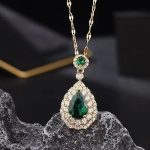 Macro shot of green pear-shaped gemstone necklace on textured dark grey stone surface
