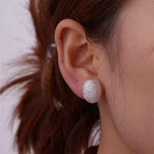Close-up of a silver matte textured teardrop stud earring worn by a model in profile