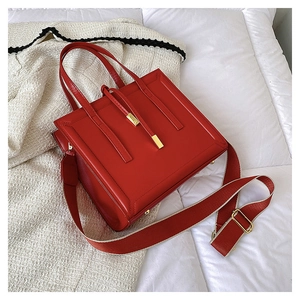 Detail of red leather crossbody bag with wide fabric strap and golden hardware